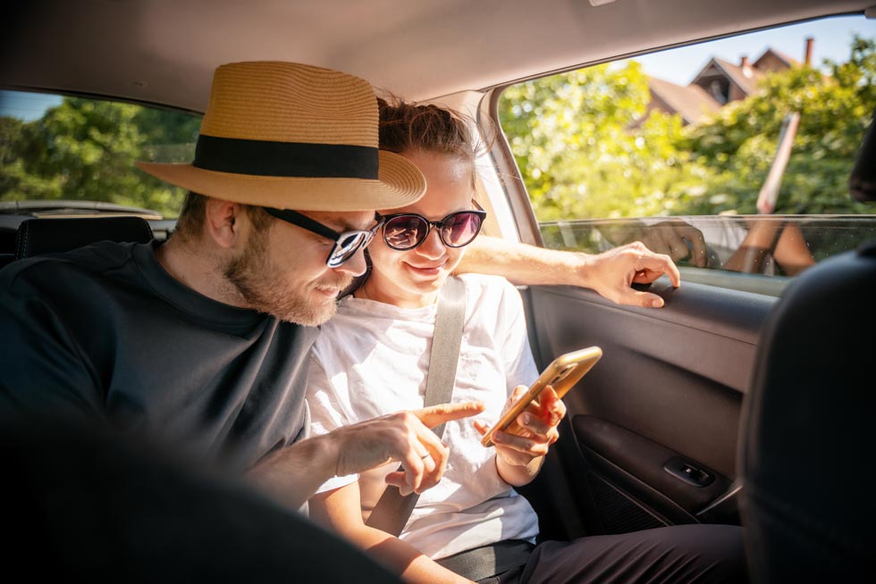 junges Pärchen sitzt in einem auto und schaut auf ein Handy